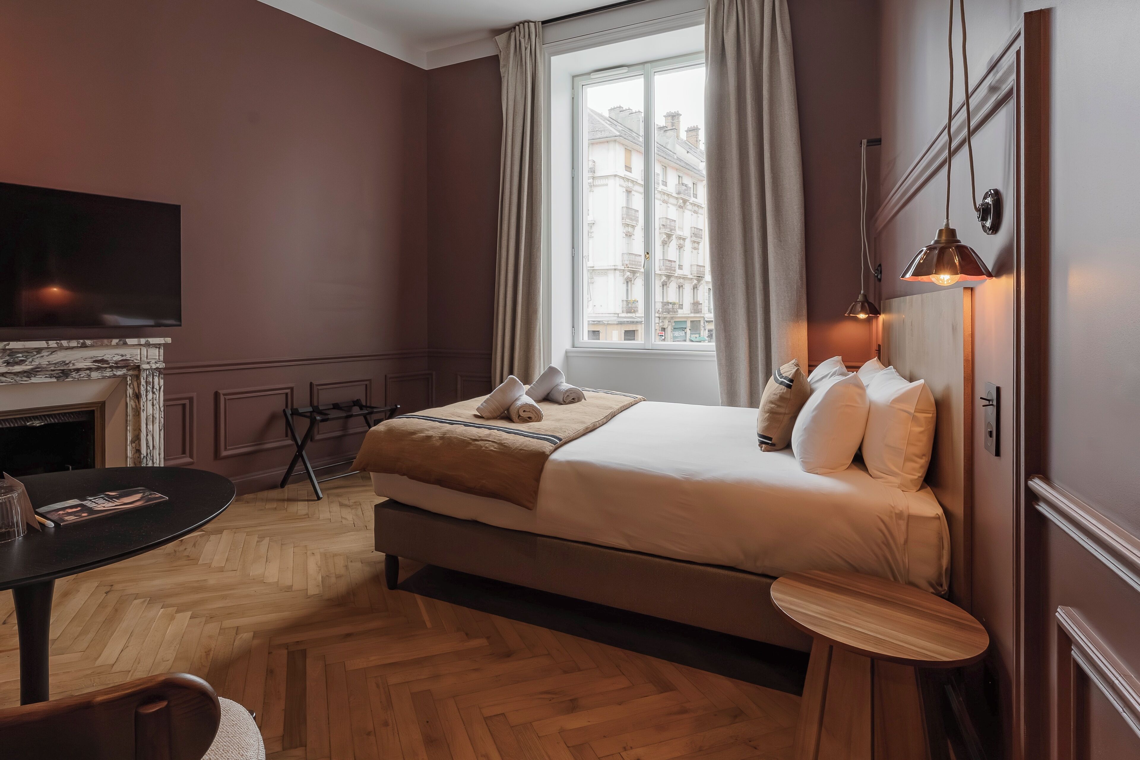 A hotel room with a bed, a TV, a small table, and a window with curtains.
