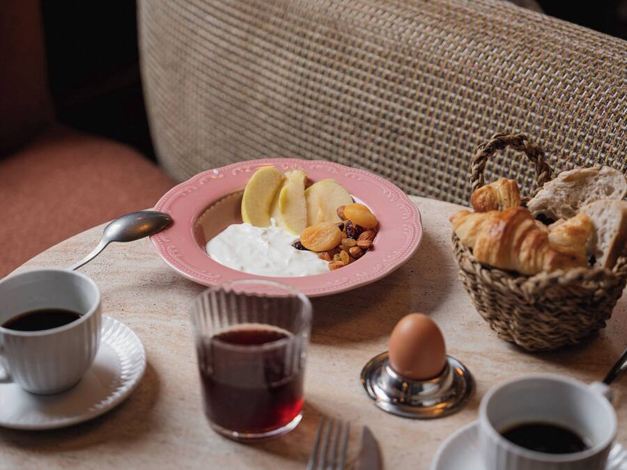 Une table mise pour le petit-déjeuner, avec une assiette de nourriture, un panier de pain et deux tasses de café.