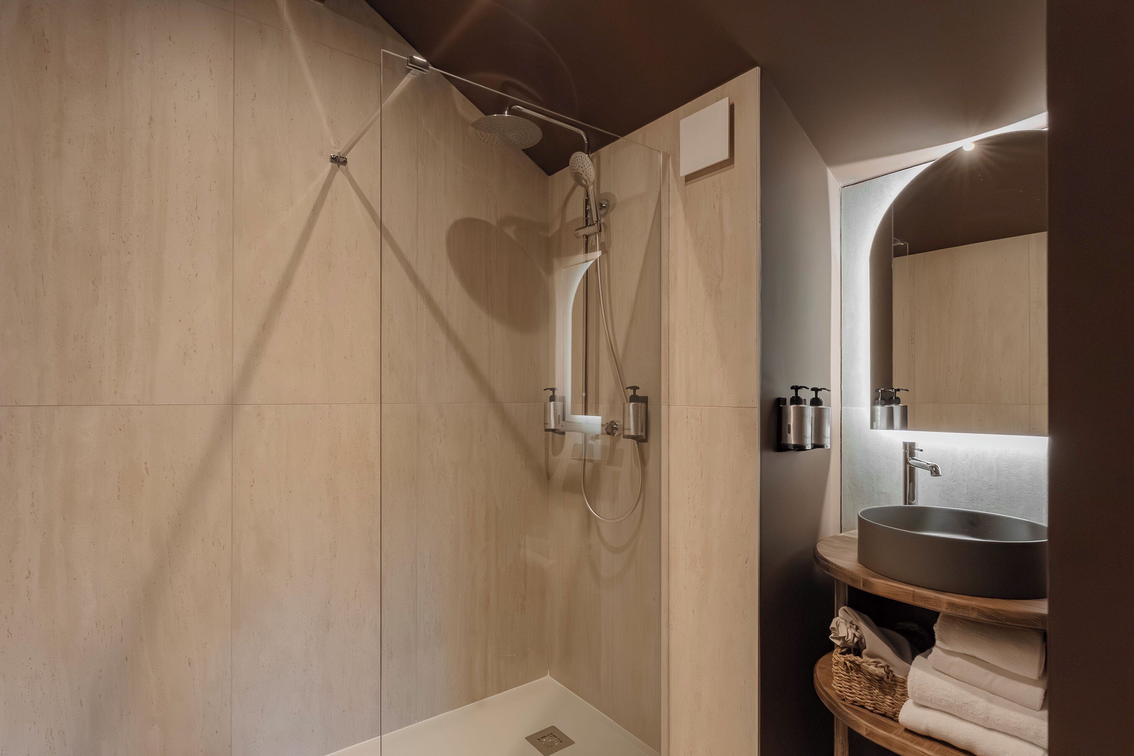 A modern bathroom with a glass-enclosed shower, a wooden vanity with a round sink, and a mirror above the sink.