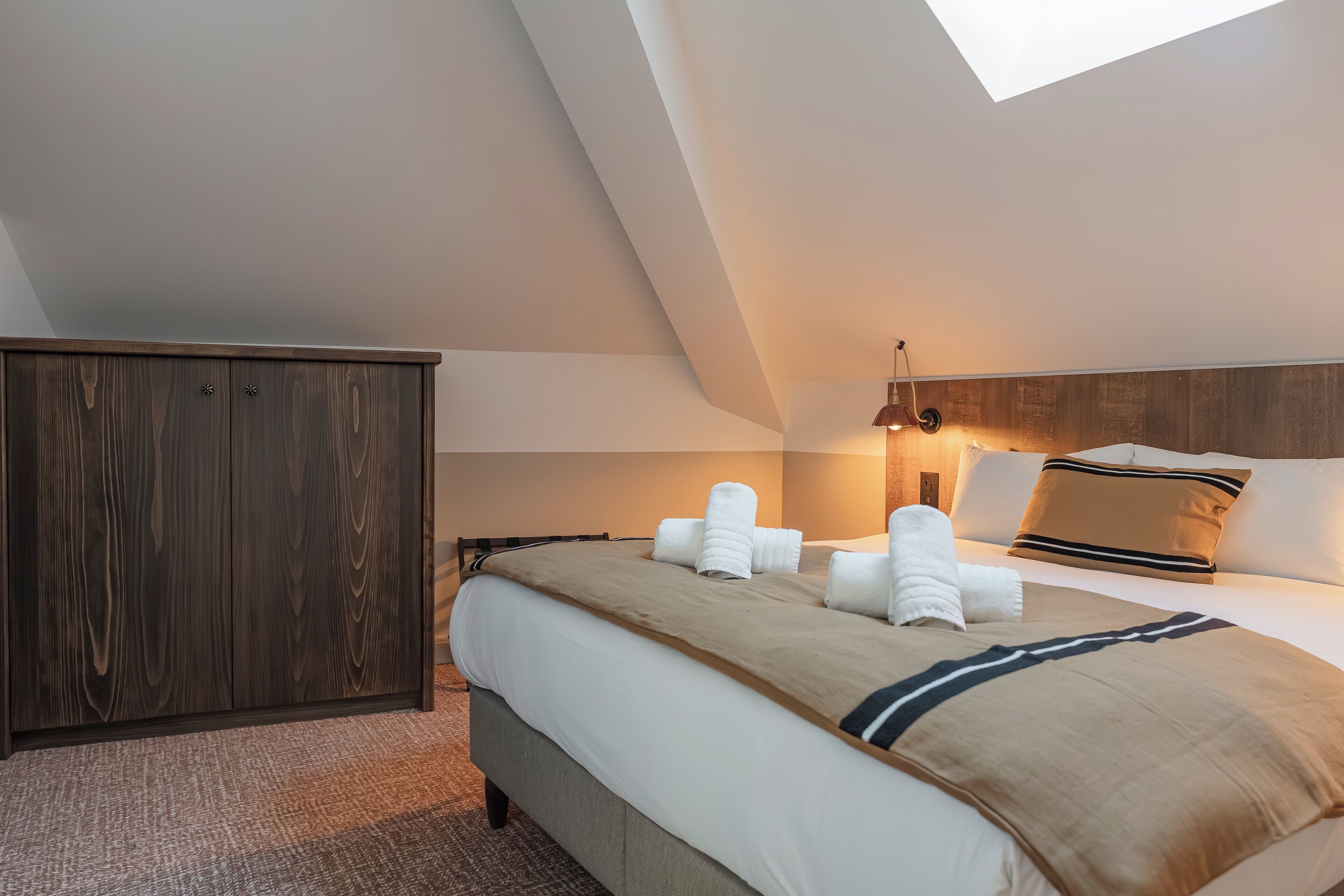A modern hotel room with a large bed, a wardrobe, and a skylight.