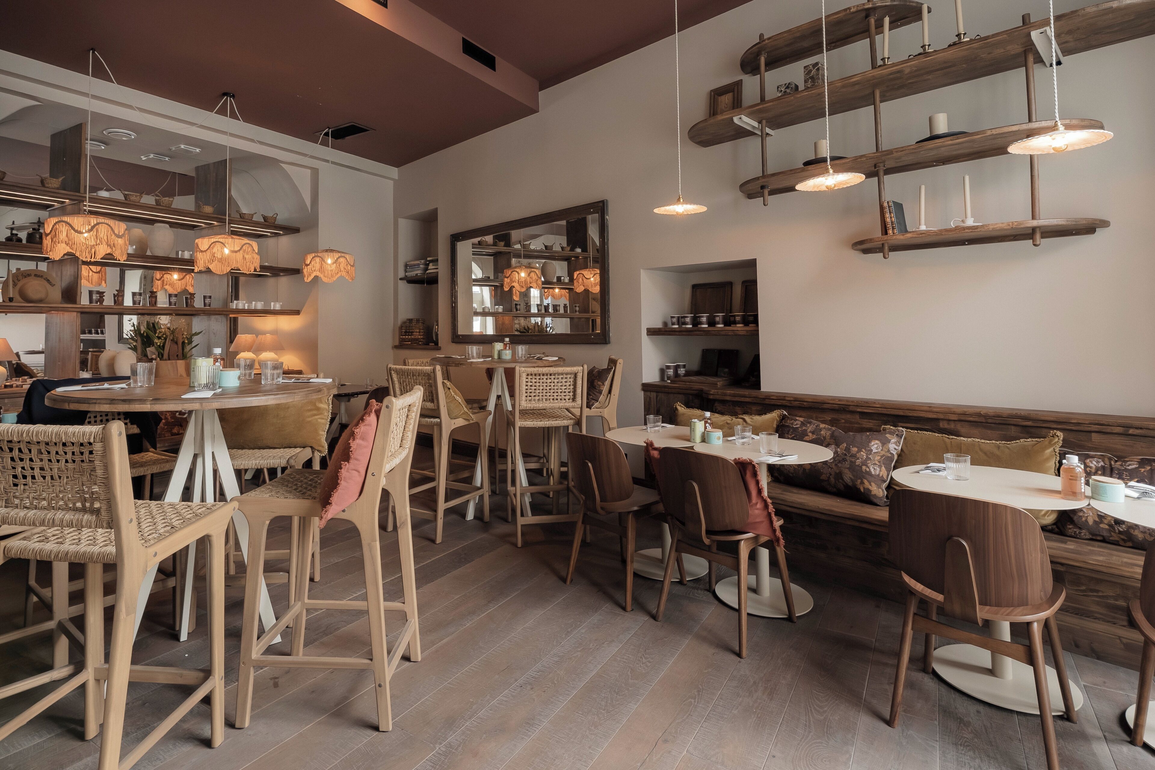 A cozy restaurant interior with wooden furniture, hanging lights, and shelves with various items.