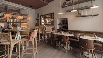 A cozy restaurant interior with wooden furniture, hanging lights, and shelves with various items.