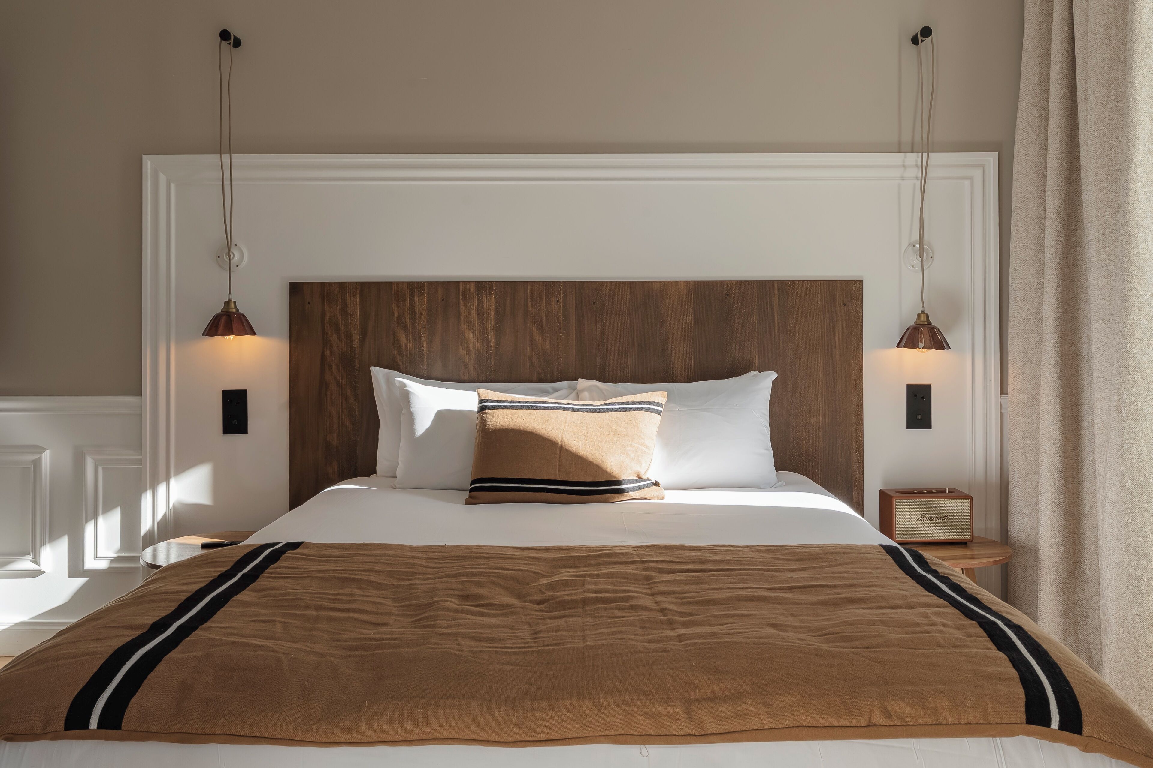 Una cama bien hecha con una manta marrón y almohadas, un cabecero de madera y dos lámparas de noche.