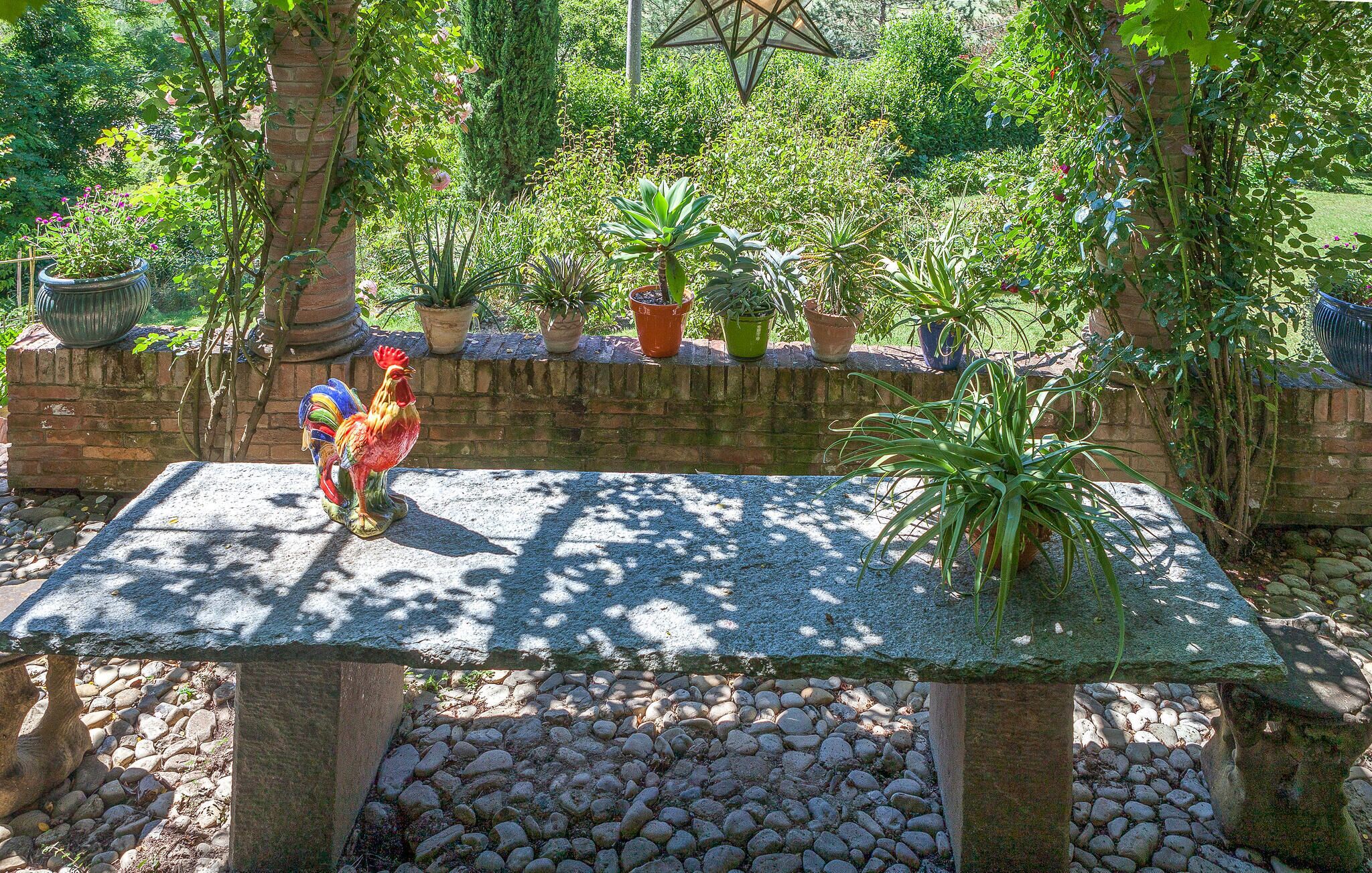 A garden with a stone bench surrounded by potted plants and a decorative rooster statue.