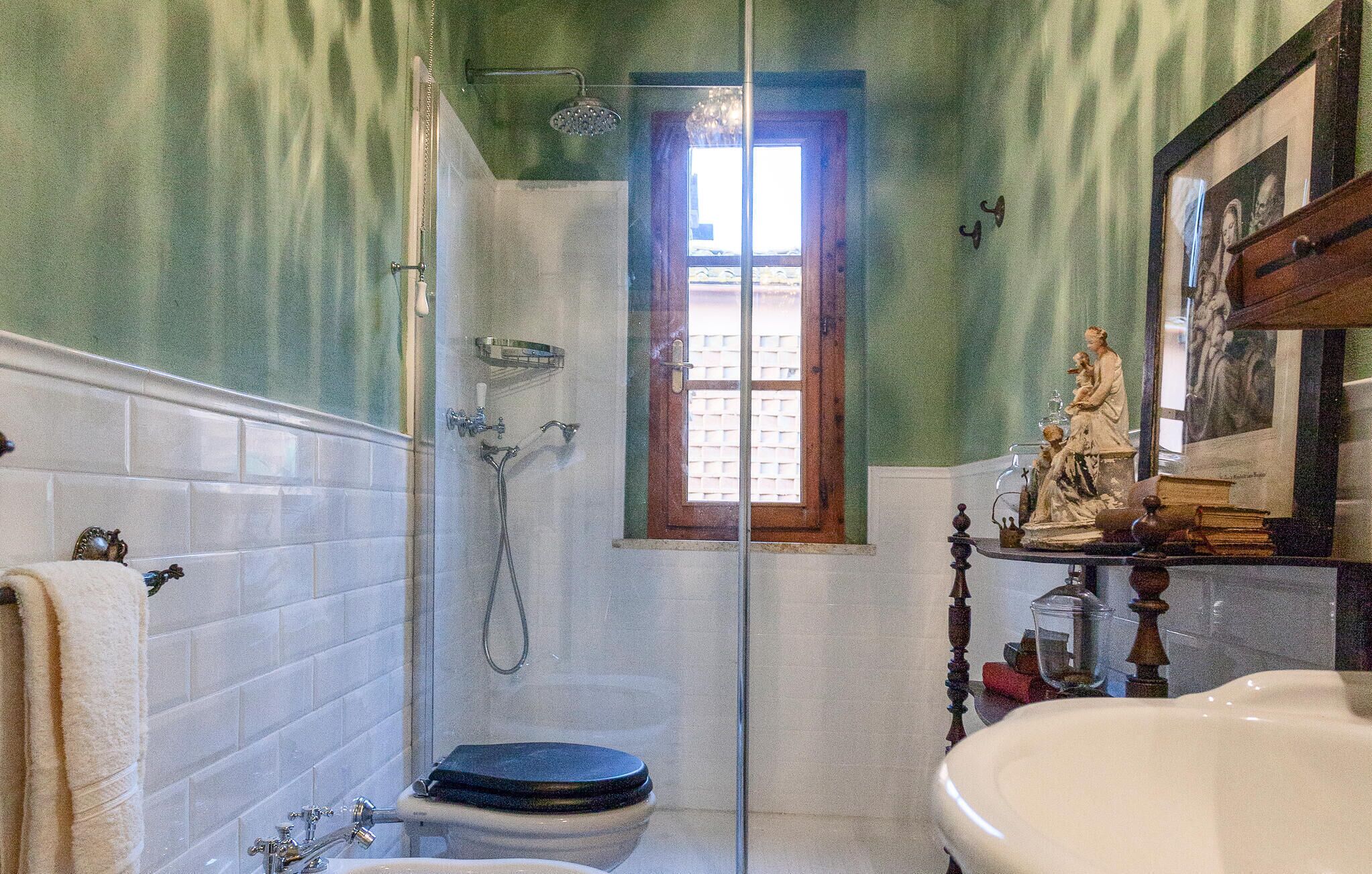 Een badkamer met een glazen douchecabine, een houten deur, een wit wastafelmeubel en een toilet met een blauwe zitting.