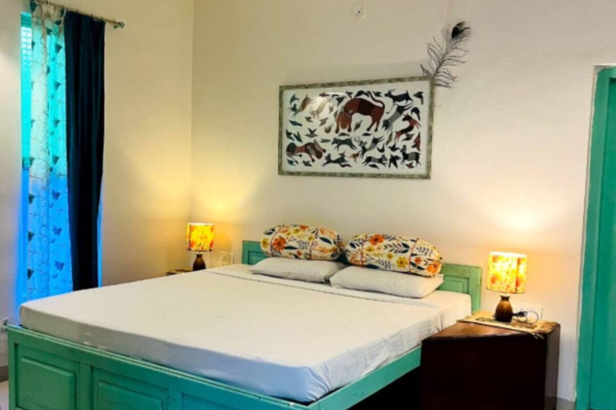 A bedroom with a turquoise bed, floral pillows, two bedside lamps, and a wall-mounted artwork of animals.