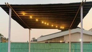 A covered outdoor seating area with a table and chairs, a volleyball, and a green fence in the background. - Tiger Safari Lodge (Ashta)