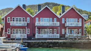 A red building with white railings and multiple windows, located near a body of water.