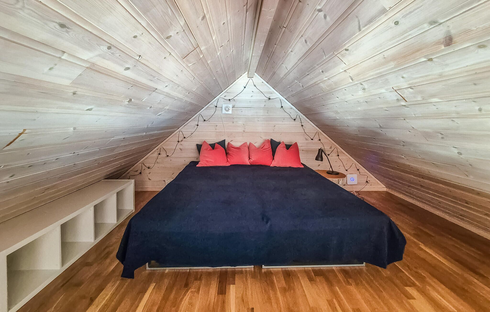Una stanza triangolare con pareti in legno e un letto con cuscini rossi.