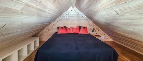 Una stanza triangolare con pareti in legno e un letto con cuscini rossi.
