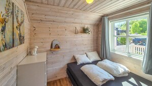 A cozy room with a bed, a small shelf with a plant, and a painting on the wall.