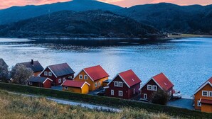 A row of colorful houses by a calm river with mountains in the background.