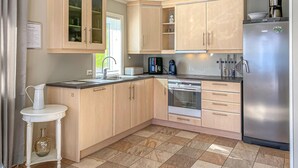 A modern kitchen with light wood cabinets, a stainless steel refrigerator, and a built-in oven.