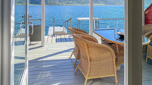 A deck with wicker furniture, a table, and a view of a lake and mountains.