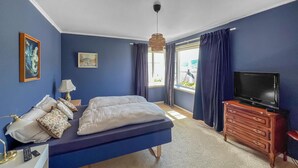 A bedroom with a bed, a dresser, a TV, and two windows with curtains.