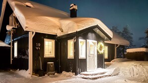 Una casa con la neve, con un numero 19, una ghirlanda sulla porta e un camino.