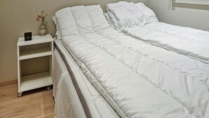 A neatly made bed with white bedding, a small bedside table with a vase of flowers, and a shelf unit with a box on it. - 4 bedroom beautiful apartment in Oslo (Oslo)