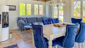 Un coin repas avec une table blanche et des chaises à coussins bleus, un lustre et une vue sur la verdure à l’extérieur.