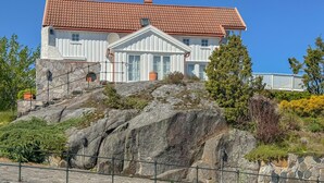 Un grand bâtiment blanc, surmonté d’un toit recouvert de tuiles rouges, situé sur le flanc d’une colline rocheuse, sous un ciel bleu dégagé.