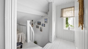 A white wooden hallway with a staircase, framed pictures on the wall, and a window with a plant. - Nice home in Tvedestrand with WiFi (Tvedestrand)
