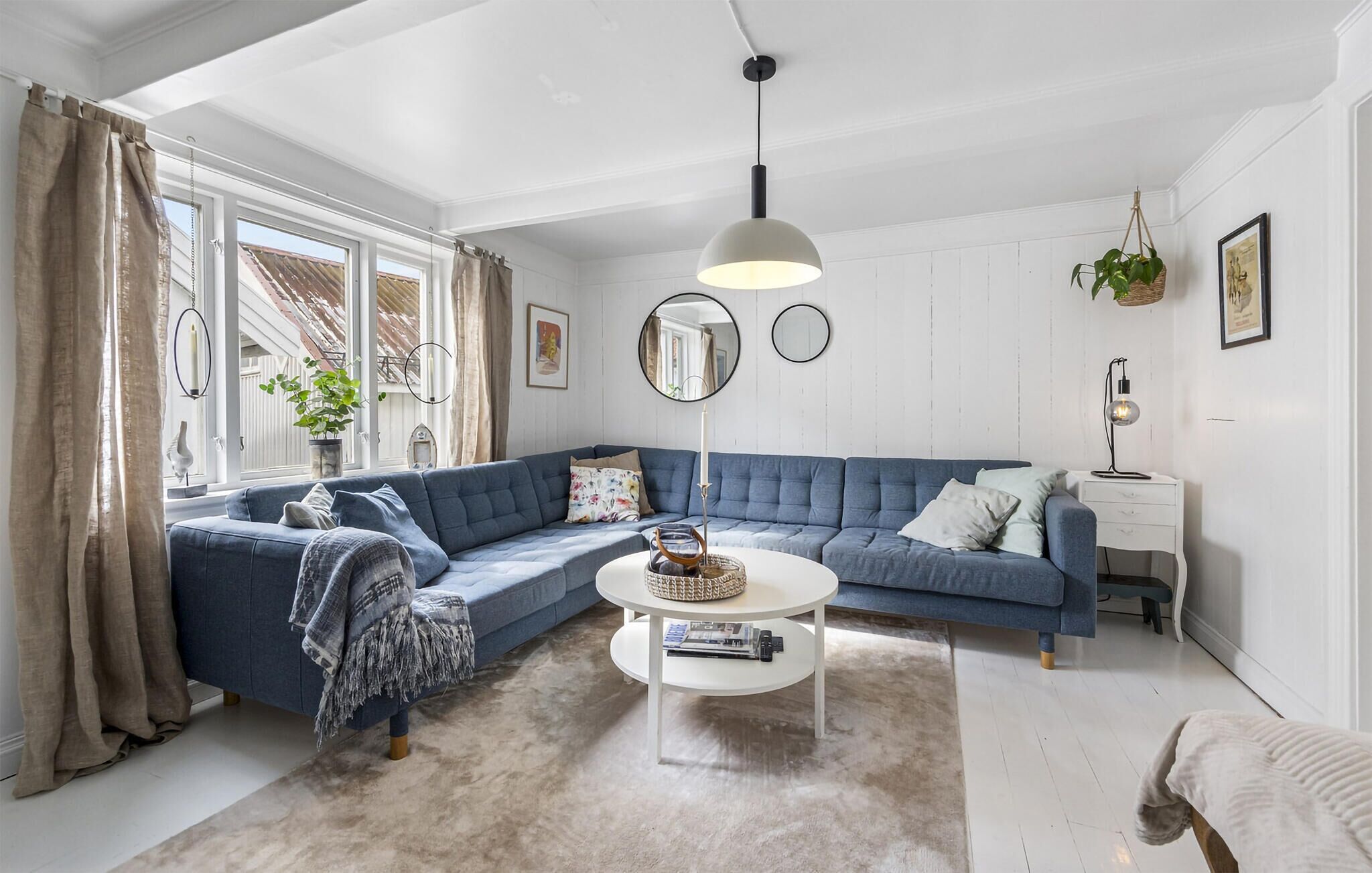 Ein modernes Wohnzimmer mit einem blauen Ecksofa, einem weißen Couchtisch und einem großen Fenster mit Vorhängen.