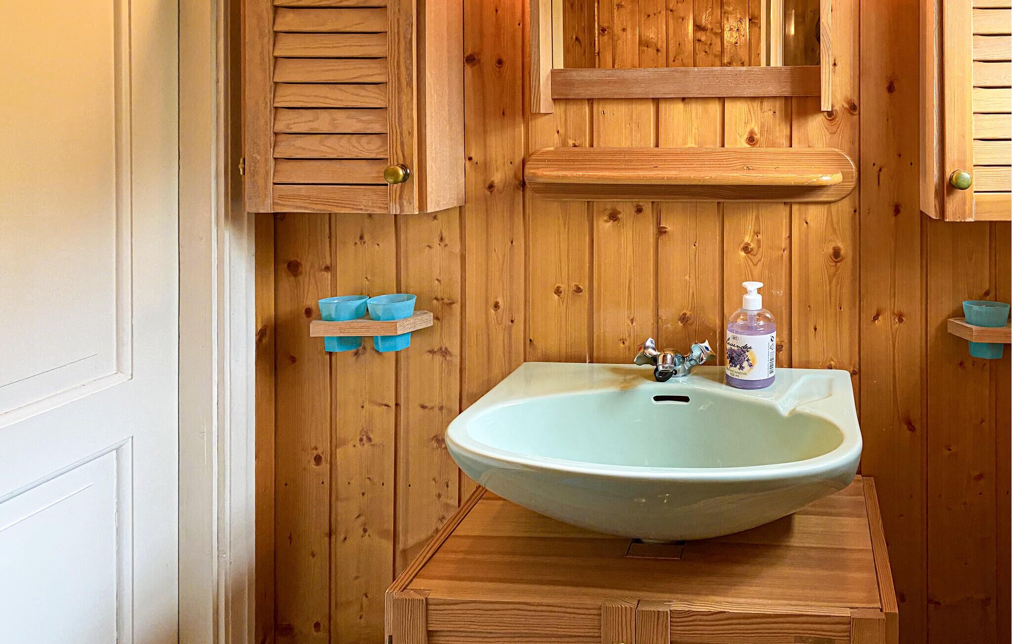 A bathroom with a wooden vanity, a sink, and a soap dispenser.