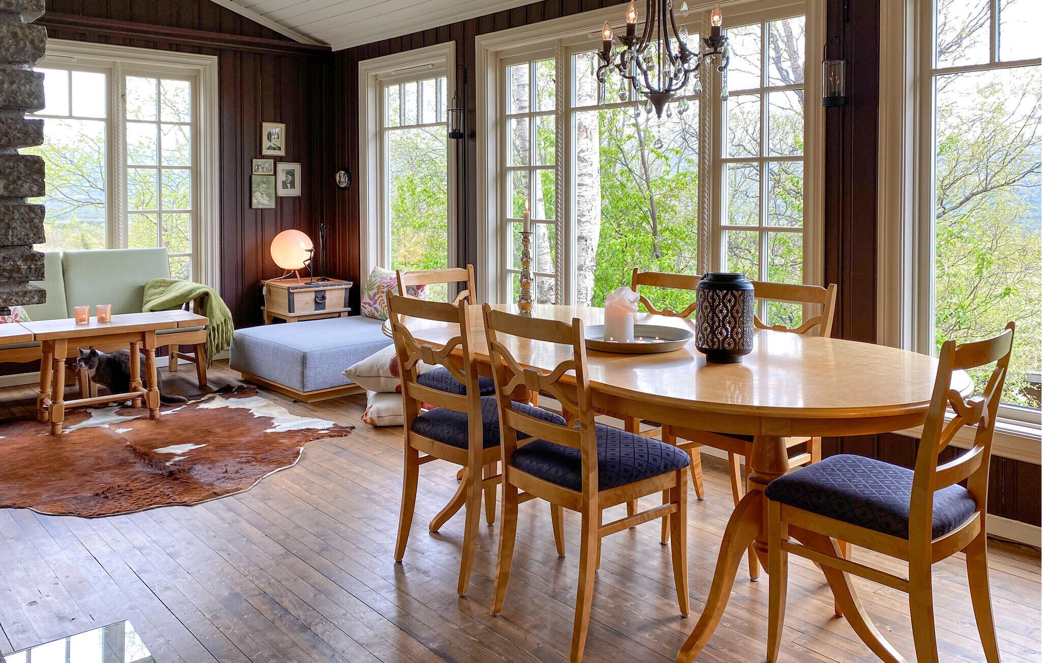 Un coin repas chaleureux avec une table et des chaises en bois, une cheminée en pierre et de grandes fenêtres donnant sur la forêt.