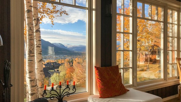 A room with a large window offering a view of a mountainous landscape and autumn foliage.