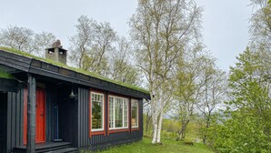 A cabin with a red door, large windows, and a grassy yard surrounded by trees.