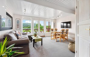 A spacious living room with a sofa, coffee table, and dining area with chairs. There is a TV mounted on the wall and a large window offering a view of the outdoors. - 2 bedroom awesome apartment in Tjørhom (Tjørhom)