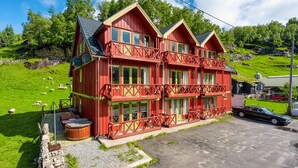 Eine rote Holzhütte mit mehreren Balkonen, gelegen an einem grünen Hügel, auf dem Schafe weiden.
