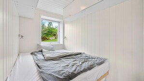 Ein Schlafzimmer mit Bett, Fenster und Blick auf Grünfläche.