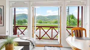Ein Zimmer mit Blick auf grüne Hügel und einen klaren Himmel. Eine hölzerne Bank und ein Tisch mit einem Stuhl sind vorhanden.