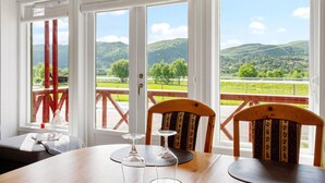 Ein Essbereich mit Tisch und Stühlen, große Fenster mit Blick auf grüne Hügel und einen klaren Himmel.