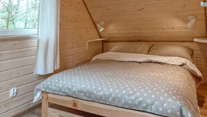 Een houten slaapkamer met een bed, een raam en een wandlamp.