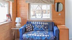 Een knus interieur met hout, een raam met uitzicht op een schommel, een tafeltje met een lamp en een blauwe, gestreepte bank.