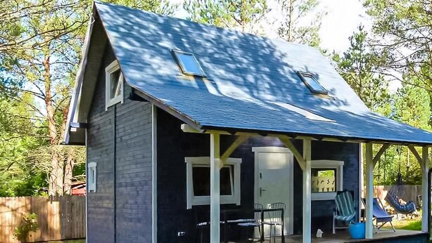 Een klein huis met een veranda, twee ramen en een overdekte zitplek buiten.