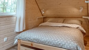 Un dormitorio de cabaña de madera con cama, ventana y lámpara de techo.