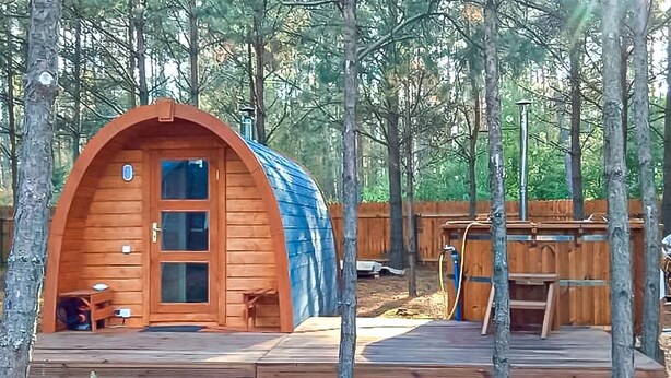 Una cabaña de madera tipo A con porche y terraza, rodeada de árboles.