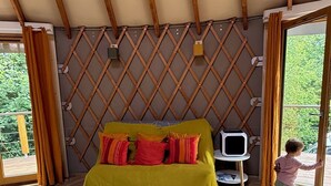 A cozy room with a bed, a TV, and a child playing near the door. - Ecolodge located in the heart of nature, between land and sea. (Arzano)