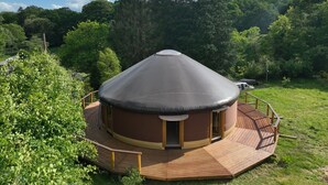 A yurt with a conical roof, surrounded by a wooden deck and a wooden fence. - Ecolodge located in the heart of nature, between land and sea. (Arzano)