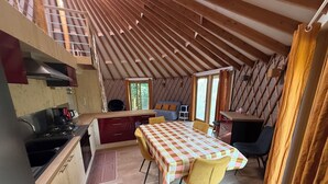 A cozy kitchen with wooden beams, a dining area with a checkered tablecloth, and a view through a window. - Ecolodge located in the heart of nature, between land and sea. (Arzano)