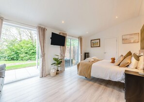 Ein Schlafzimmer mit einem Bett, einem Fernseher, einem großen Fenster und Blick auf Grünfläche.