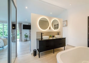 Un baño moderno con una bañera grande, un tocador doble y un espejo grande con iluminación circular.