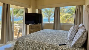 A bedroom with a large bed, a television on a wooden cabinet, and a view of the beach through large windows. - Hermoso espacio a pie de playa y alberca By Gps (Mazatlan)