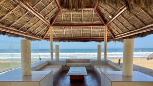 A beachside lounge with a thatched roof, a wooden bench, and a view of the ocean. - Hermoso espacio a pie de playa y alberca By Gps (Mazatlan)