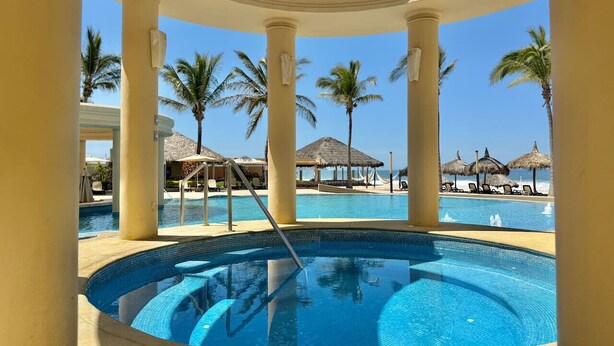 A circular pool with a clear blue water, surrounded by white columns and palm trees. - Hermoso espacio a pie de playa y alberca By Gps (Mazatlan)