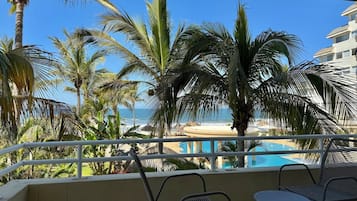 Varanda com vista para uma piscina e praia, rodeada por palmeiras.