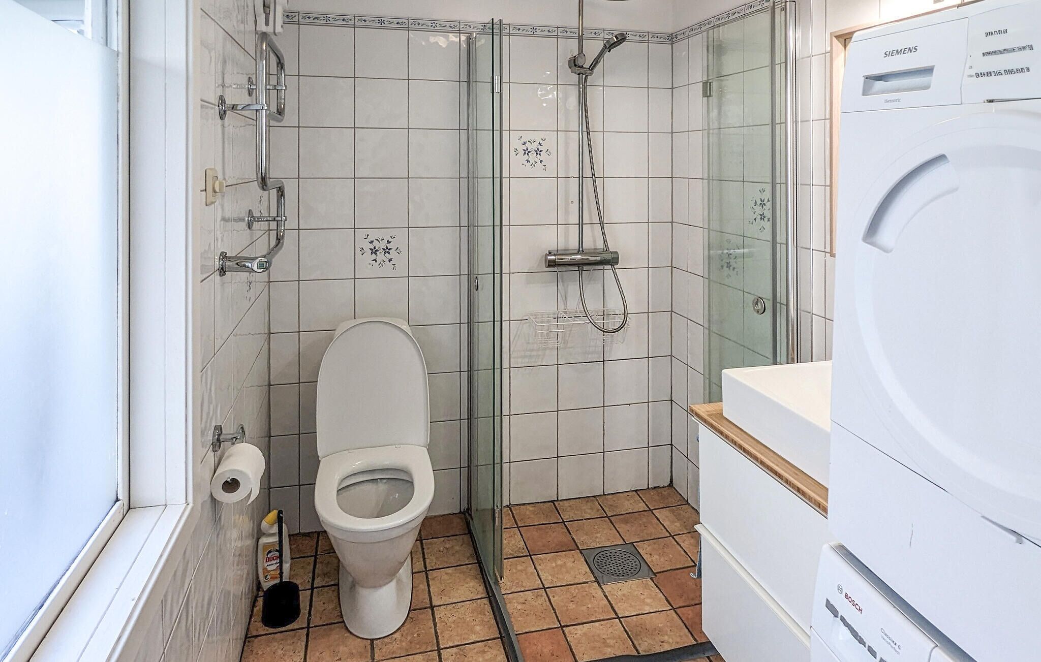 A bathroom with a toilet, a shower, and a washing machine.