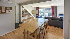 A modern living space with a wooden dining table, white chairs, a grey sofa, and a staircase leading to another level. - Gorgeous home in Hovås with WiFi (Hovås)